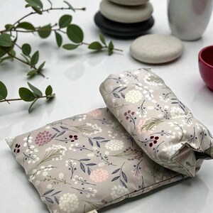 Puede incluir: Se muestran dos almohadillas t&eacute;rmicas grises con estampado floral, una rectangular y otra cil&iacute;ndrica. Las almohadillas presentan un patr&oacute;n de flores blancas, rosas y burdeos con hojas verdes. Las almohadillas est&aacute;n sobre una superficie blanca.