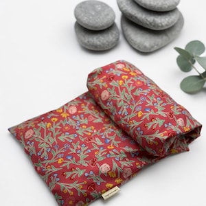 Puede incluir: Dos almohadas rojas con estampado floral, una doblada, con un patr&oacute;n de flores y hojas amarillas, azules y rosas. Piedras grises y una ramita de vegetaci&oacute;n en el fondo. Las almohadas tienen una etiqueta que dice "Higher Designs".