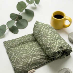 Puede incluir: Una almohada y un coj&iacute;n enrollado con estampado floral verde, junto a una taza de caf&eacute; amarilla y una ramita de eucalipto. La almohada y el coj&iacute;n est&aacute;n hechos de tela con un patr&oacute;n bot&aacute;nico repetido.