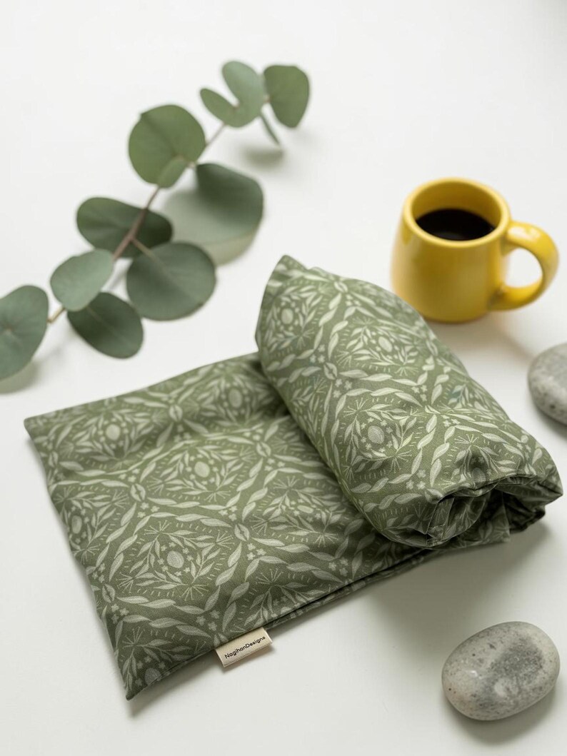 Puede incluir: Una almohada y un coj&iacute;n enrollado con estampado floral verde, junto a una taza de caf&eacute; amarilla y una ramita de eucalipto. La almohada y el coj&iacute;n est&aacute;n hechos de tela con un patr&oacute;n bot&aacute;nico repetido.