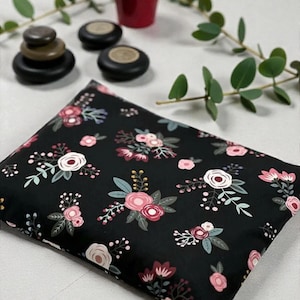 K&ouml;nnte beinhalten: Ein schwarzes rechteckiges Kissen mit einem Blumenmuster aus rosa und wei&szlig;en Rosen, gr&uuml;nen Bl&auml;ttern und Beeren. Das Bild zeigt auch einen kleinen roten Topf, gestapelte Steine und Zweige mit Gr&uuml;n.