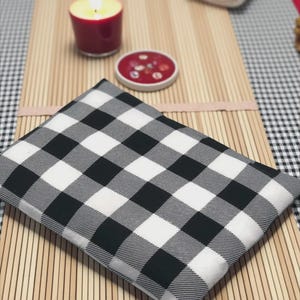 May include: A rectangular fabric pouch featuring a black and white buffalo check pattern. The pouch is constructed from a woven textile material and displays a consistent grid design across its entire visible surface area.