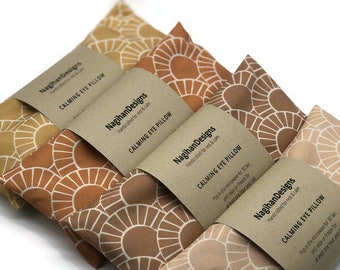 Puede incluir: Una colección de almohadas calmantes para los ojos en varios tonos de marrón y beige, cada una con un patrón de rayos de sol único. Las almohadas están etiquetadas como "CALMING EYE PILLOW" y "NagihanDesigns". La imagen sugiere relajación y bienestar.