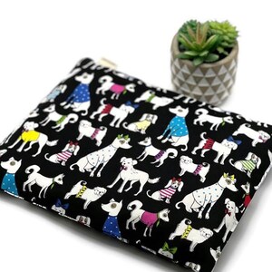 K&ouml;nnte beinhalten: Schwarze Rei&szlig;verschlusstasche mit einem sich wiederholenden Muster aus wei&szlig;en Hunden in verschiedenen Outfits. Die Hunde tragen Pullover, Fliegen und Polka-Dot-Hemden. Ein kleiner Topf mit Sukkulenten befindet sich im Hintergrund.