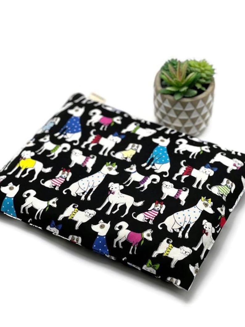 K&ouml;nnte beinhalten: Schwarze Rei&szlig;verschlusstasche mit einem sich wiederholenden Muster aus wei&szlig;en Hunden in verschiedenen Outfits. Die Hunde tragen Pullover, Fliegen und Polka-Dot-Hemden. Ein kleiner Topf mit Sukkulenten befindet sich im Hintergrund.