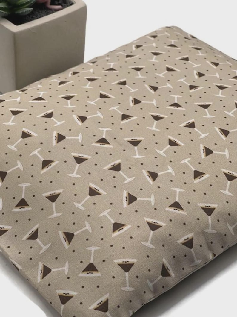 K&ouml;nnte beinhalten: Ein beiges Kissen mit einem sich wiederholenden Muster aus braunen Martinigl&auml;sern und kleinen braunen Punkten. Das rechteckige Kissen ist aus Stoff gefertigt. Das Design ist gleichm&auml;&szlig;ig &uuml;ber die Oberfl&auml;che verteilt.