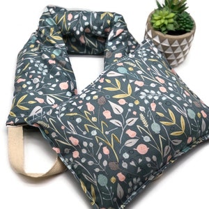 May include: A dark teal neck wrap featuring a repeating botanical pattern of pink, yellow, and light blue flowers, leaves, and berries. The fabric wrap includes a beige fabric handle attached to one side for easy carrying and positioning.