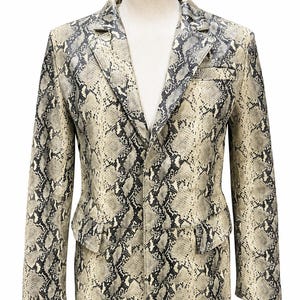 May include: A blazer featuring a beige and black snakeskin pattern throughout. The garment includes a notched lapel, a single-breasted front closure, long sleeves, and two flap pockets positioned at the lower front, displayed on a mannequin.