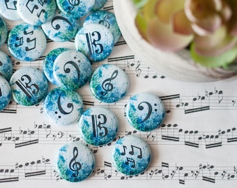 May include: A collection of round, blue and green patterned paper circles with musical notes and symbols printed on them. The circles are scattered on a white surface with musical notes printed on it.