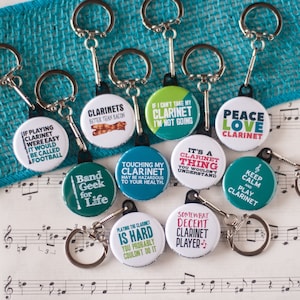 May include: Ten colorful keychains with different clarinet-themed sayings. The keychains are on a sheet of music with a turquoise background.