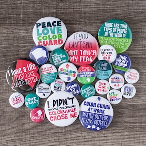 May include: A collection of colorful round buttons with various slogans related to color guard. The slogans include "Peace Love Color Guard", "If You Can't Spin Don't Touch My Flag", "I Have A Life Just Like Guard Better", "Color Guard Watch Out For Flying Objects", and more.