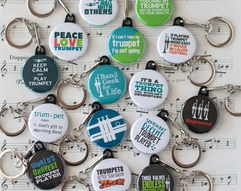 Puede incluir: Una colección de 12 llaveros coloridos con diferentes diseños con temática de trompeta. Los llaveros presentan frases como "Plays Well With Others", "Peace Love Trumpet", "Keep Calm and Play Trumpet", "Band Geek for Life", "It's a Trumpet Thing", "If Playing Trumpet Were Easy", "Some What Decent Trumpet Player", "World's Okayest Trumpet Player", "Trumpets Better Than Bacon", "Three Valves Endless Possibilities", y "Represent".