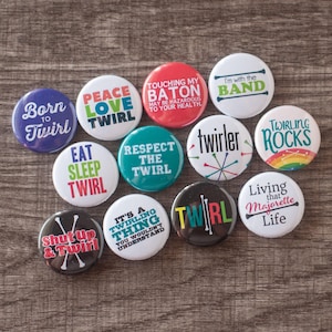 Può includere: Una collezione di bottoni rotondi con varie frasi e grafiche relative al twirling. I bottoni sono in diversi colori, tra cui blu, rosso, verde e bianco, con testi come "Born to Twirl" e "Twirling Rocks".