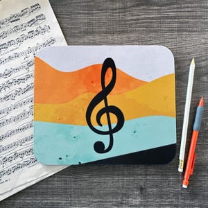May include: A black treble clef on a colorful mousepad with a watercolor-like design of orange, yellow, and blue waves.