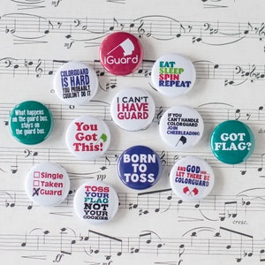 May include: Ten colorful round buttons with various sayings related to color guard. The buttons are on a sheet of music with musical notes and a treble clef.