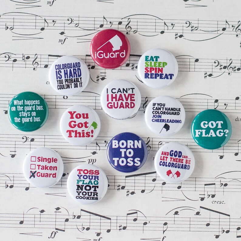 May include: Ten colorful round buttons with various sayings related to color guard. The buttons are on a sheet of music with musical notes and a treble clef.