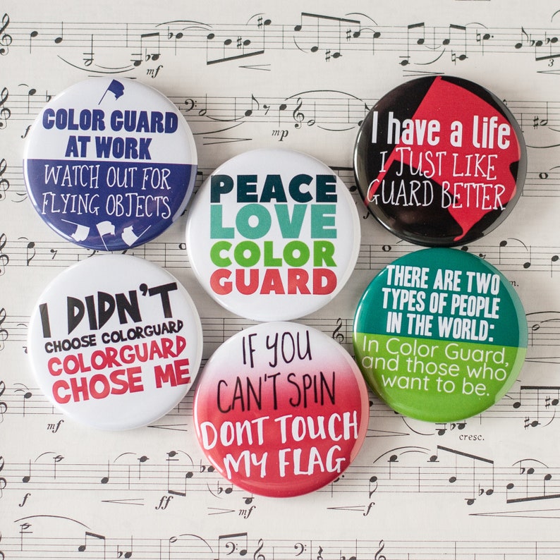 May include: Nine colorful round buttons with different slogans related to color guard. The slogans include "Color Guard at Work", "Peace Love Color Guard", "I Didn't Choose Colorguard Colorguard Chose Me", "If You Can't Spin Don't Touch My Flag", "I Have a Life I Just Like Guard Better", and "There Are Two Types of People in the World: In Color Guard, and Those Who Want to Be."