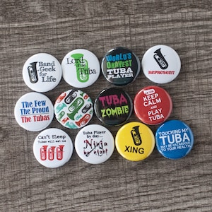 Könnte beinhalten: Eine Sammlung von 10 runden Knöpfen mit verschiedenen Tuba-Designs. Die Knöpfe zeigen Sätze wie "World's Okayest Tuba Player", "Tuba Zombie", "Keep Calm and Play Tuba" und "Touching My Tuba May Be Hazardous to Your Health".