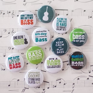 May include: Ten round, colorful buttons with humorous sayings about playing the bass guitar. The buttons are on a sheet of music.