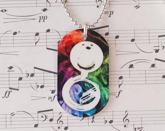 May include: A silver necklace with a pendant showing a white French horn design against a rainbow smoke background. The pendant is rectangular with curved edges. The background is musical notation.