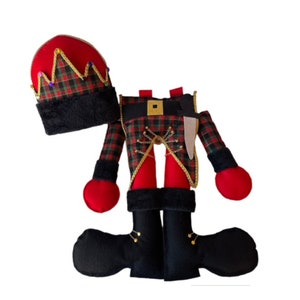 May include: A red and green plaid nutcracker doll with a black hat and boots. The doll is wearing a gold belt and has a sword on its side.