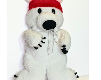 May include: A plush polar bear figure with a red hat, black eyes, and a black nose. The bear has white fur and black claws on its paws. A silver ribbon is tied around its neck. The bear is standing upright.