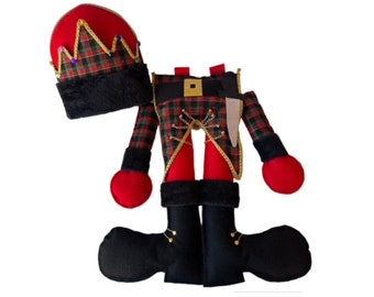 May include: A red and green plaid nutcracker doll with a black hat and boots. The doll is wearing a gold belt and has a sword on its side.