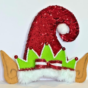 May include: A festive elf hat with a red sequined cap and a white pom-pom. The hat features green felt trim with white edging, a red and white striped bow, and tan felt ears. A fun accessory for the holidays.
