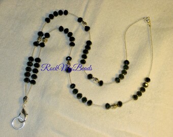 May include: A black beaded lanyard with silver accents and a silver clasp. The lanyard is made of two strands of beads, with a larger rectangle of beads in the center. The text "Rock My Beads" is visible in the image.