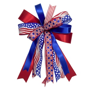 May include: A patriotic bow featuring red, white, and blue ribbons. The bow includes ribbons with American flags, stars, and stripes patterns. The bow is suitable for decorating wreaths, gifts, or other crafts.