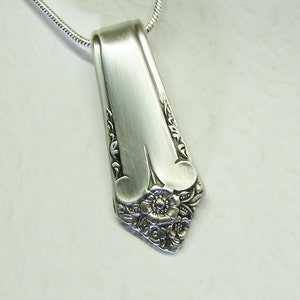 May include: A silver necklace with a pendant made from a vintage silverware piece. The pendant features a floral design with a central flower and intricate details.