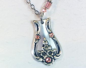 May include: A silver-toned metal pendant crafted from a repurposed spoon handle, featuring an embossed floral design at the base. The pendant is accented with three small, round, light pink crystals and hangs from a silver-toned chain with pink beads.