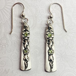 May include: Silver earrings with a floral design and green gemstones. The earrings are made from repurposed silverware.