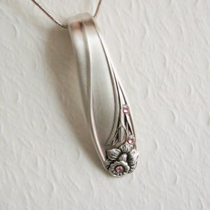 May include: A silver spoon pendant necklace with a floral design and pink rhinestones. The pendant is shaped like a teardrop and has a smooth, polished finish.