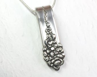 May include: A silver-toned pendant crafted from a repurposed spoon handle, featuring an embossed floral pattern with multiple blossoms and leaves. The pendant is suspended from a thin, flexible silver-toned snake chain necklace.