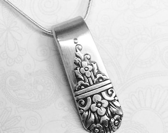 May include: A silver-toned pendant crafted from a repurposed spoon handle, featuring an embossed floral pattern with intricate leaves and blossoms. The pendant is suspended from a thin, flexible silver-toned snake chain necklace.
