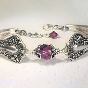 Könnte beinhalten: Ein Armband aus einem silbernen Löffel mit einer violetten Kristallperle. Der Löffel hat ein Traubenmuster und auf der Rückseite sind die Worte "1947 Rogers England" eingraviert.