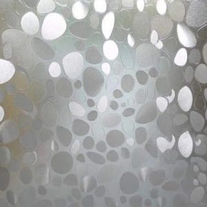May include: A frosted window film with a pebble design. The film features a pattern of irregularly shaped, opaque, gray and white stones. The design is repeated across the surface, creating a textured, decorative effect. The film is likely used for privacy or decorative purposes.