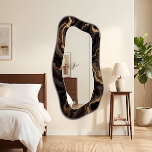Puede incluir: Un espejo de pared de cuerpo entero con una forma orgánica irregular y un marco que presenta un patrón de mármol arremolinado en tonos negro, marrón oscuro y oro metálico. La superficie reflectante muestra una vista clara de la habitación.