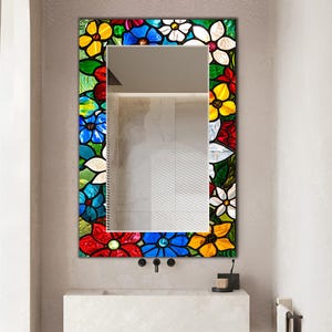 May include: A rectangular wall mirror featuring a decorative border made of colorful stained glass pieces arranged in a floral pattern. The glass elements include vibrant red, blue, yellow, green, and white petals with dark outlines.