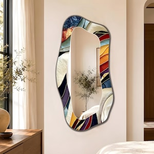 May include: An irregular, organic-shaped wall mirror featuring a wide, decorative border with layered, abstract patterns in vibrant shades of red, orange, yellow, blue, and white, surrounding a clear, reflective central glass surface.
