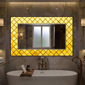 May include: A rectangular mirror with a yellow, diamond-patterned frame hangs above a white bathtub. The mirror reflects a window and a dark interior. The bathroom features marble-effect walls and gold-toned fixtures, creating a luxurious spa-like atmosphere.