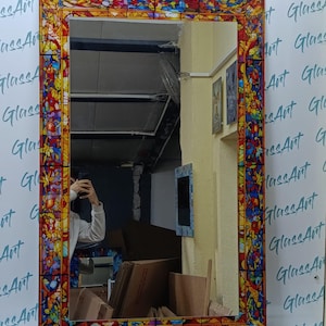 K&ouml;nnte beinhalten: Rechteckiger Spiegel mit einem Buntglasrand. Der Rand weist ein farbenfrohes Blumenmuster mit roten, blauen, gelben und orangen Farbt&ouml;nen auf. Der Spiegel wird vor einer wei&szlig;en Wand mit dem Text "GlassArt" wiederholt angezeigt.