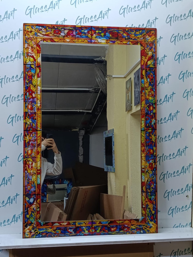 K&ouml;nnte beinhalten: Rechteckiger Spiegel mit einem Buntglasrand. Der Rand weist ein farbenfrohes Blumenmuster mit roten, blauen, gelben und orangen Farbt&ouml;nen auf. Der Spiegel wird vor einer wei&szlig;en Wand mit dem Text "GlassArt" wiederholt angezeigt.