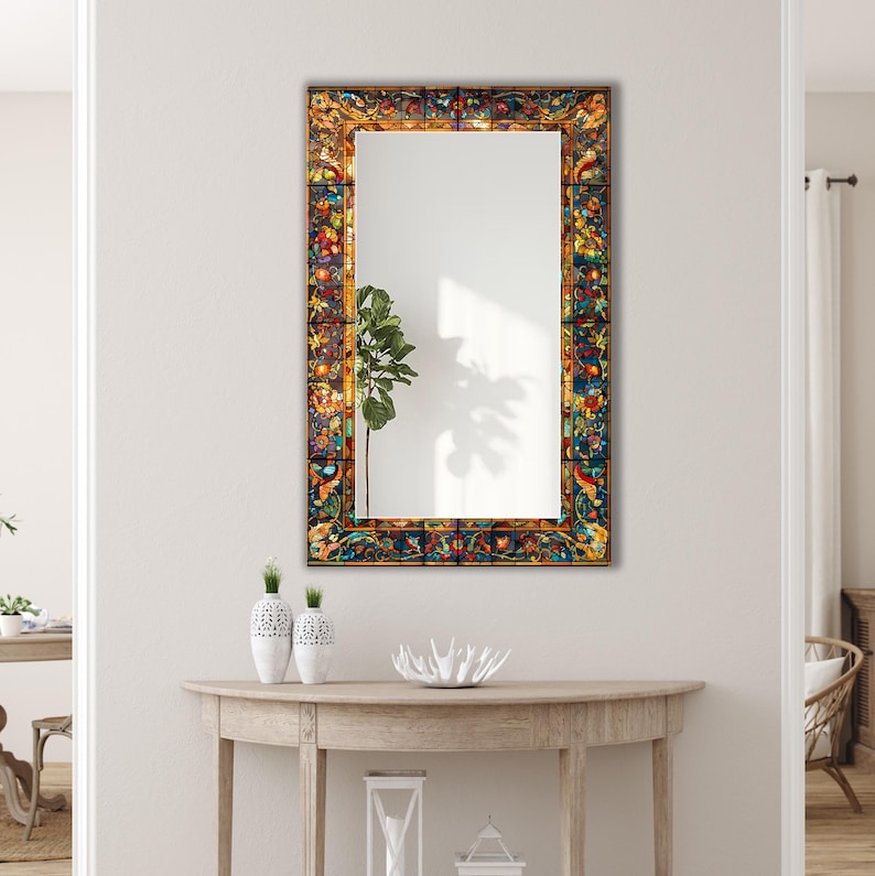 K&ouml;nnte beinhalten: Rechteckiger Wandspiegel mit einem Rahmen im Glasmalerei-Stil. Der Rahmen weist ein farbenfrohes Blumen- und geometrisches Design mit Rot-, Blau-, Gelb- und Gr&uuml;nt&ouml;nen auf. Der Spiegel h&auml;ngt an einer wei&szlig;en Wand.