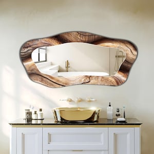 Puede incluir: Un espejo de pared con un marco de forma orgánica irregular y un patrón detallado de vetas de madera marrón. La superficie reflectante muestra el interior de un baño con una bañera blanca, un grifo dorado y un lavabo dorado.