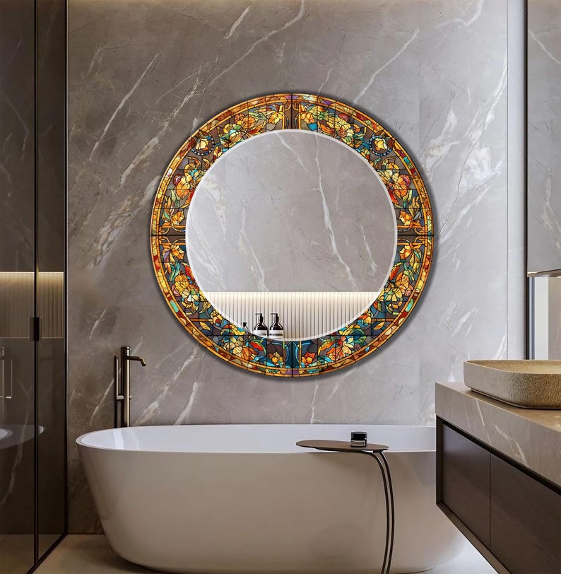 K&ouml;nnte beinhalten: Ein runder Buntglasspiegel mit farbenfrohem Blumenmuster. Der Rahmen ist ein Mosaik aus Orange, Gelb, Blau und Gr&uuml;n. Der Spiegel h&auml;ngt an einer grauen Marmorwand &uuml;ber einer wei&szlig;en Badewanne.