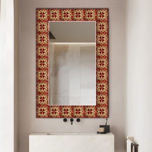 May include: A rectangular wall mirror featuring a decorative frame with a repeating pattern of dark red four-leaf clover shapes set against a cream-coloured background with gold-toned accents, surrounding a clear, reflective glass surface.