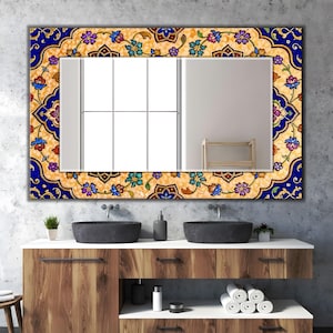 May include: Rectangular mirror with a decorative floral border in shades of blue, yellow, and purple. The mirror is mounted above a wooden vanity with black sinks and a white countertop. The mirror's frame features an intricate floral design.