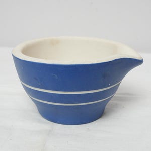 May include: A blue ceramic bowl with a white interior and a spout. The bowl has two white stripes around the exterior. The bowl is sitting on a white surface.
